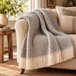 Hoop Pattern Grey Wool Blanket with a cream fringe draped over a cream boucle sofa beside a rustic wooden side table, jute rug and a vase of greenery
