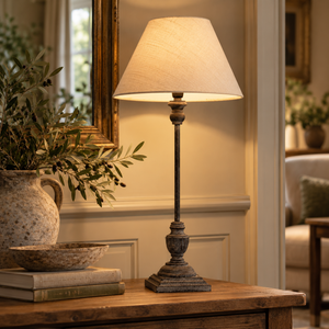 Incia Wooden Table Lamp in the Stem style, lit on a wooden chest beside olive branches in a stoneware jug