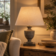 Incia Wooden Table Lamp in the Urn style, lit on a wooden side table beside a sofa