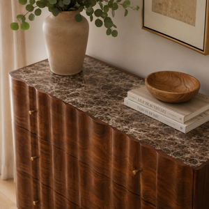 Wooden chest of drawers with marble top, vase, and books in a home setting