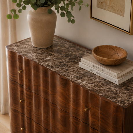 Wooden chest of drawers with marble top, vase, and books in a home setting
