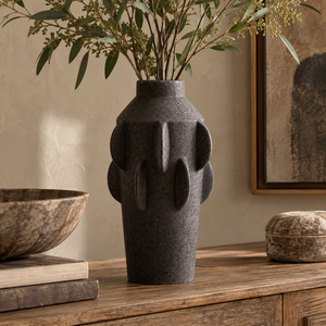 Iona Black Textured Stoneware Large Vase with its sculpted finned profile, filled with green eucalyptus branches, displayed on a rustic wooden console table in a warm, styled interior setting.