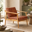 The Jakarta Brown Leather with Natural Teak Wood Armchair on a jute rug beside a carved wooden side table in a sunlit living room.