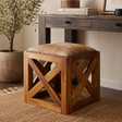 Wooden stool with hair-on goat leather seat in a room setting with a desk and plant.