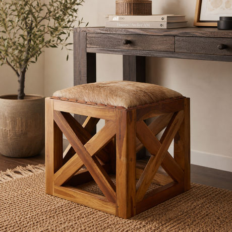 Wooden stool with hair-on goat leather seat in a room setting with a desk and plant.