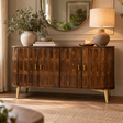 A mid-century modern wooden sideboard cabinet with a textured oval pattern, styled in a warm, elegant room with a lamp, books, and a vase of greenery.