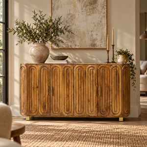 A mid-century modern wooden sideboard with a carved arched panel design, styled in a warm, sunlit living room with a large ceramic vase, candles, and wall art.