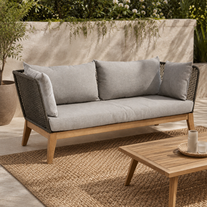 Woven sofa with gray cushions and wooden frame on a patio with a coffee table.
