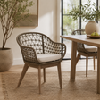 Wicker chair with a cushion in a room with a wooden table and plants.