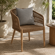 Wicker chair with a gray cushion on a patio with plants and a small table.