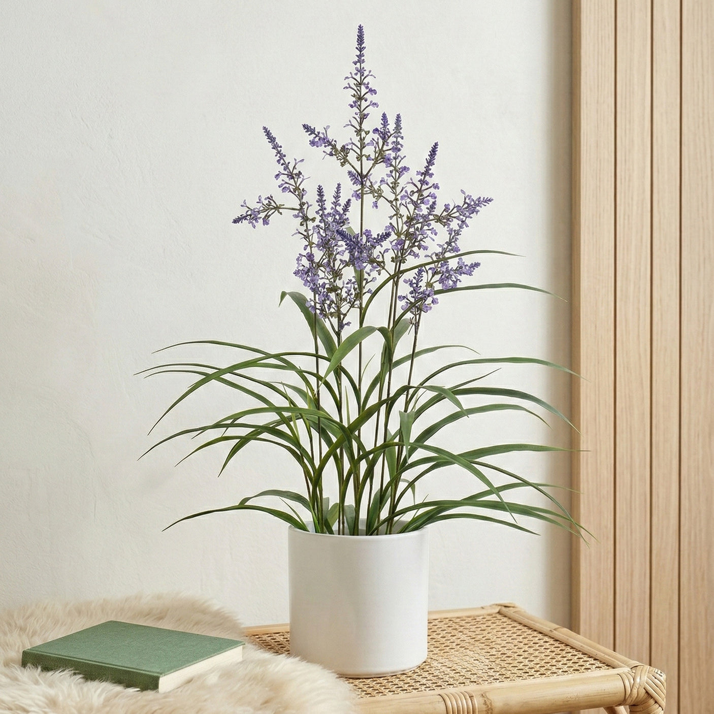 Artificial lavender plant with delicate purple flowers and green foliage in a white pot, styled on a natural rattan tray indoors.