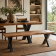 A rustic wooden dining table with a live-edge top and black X-shaped metal legs, paired with a matching wooden bench in a styled dining room setting.