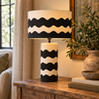 Luma Black And White Curved Stripe Papier Mache Table Lamp lit on a wooden console beside olive branches
