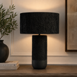 Luma black papier mache table lamp on a wooden table with decor items against a beige wall