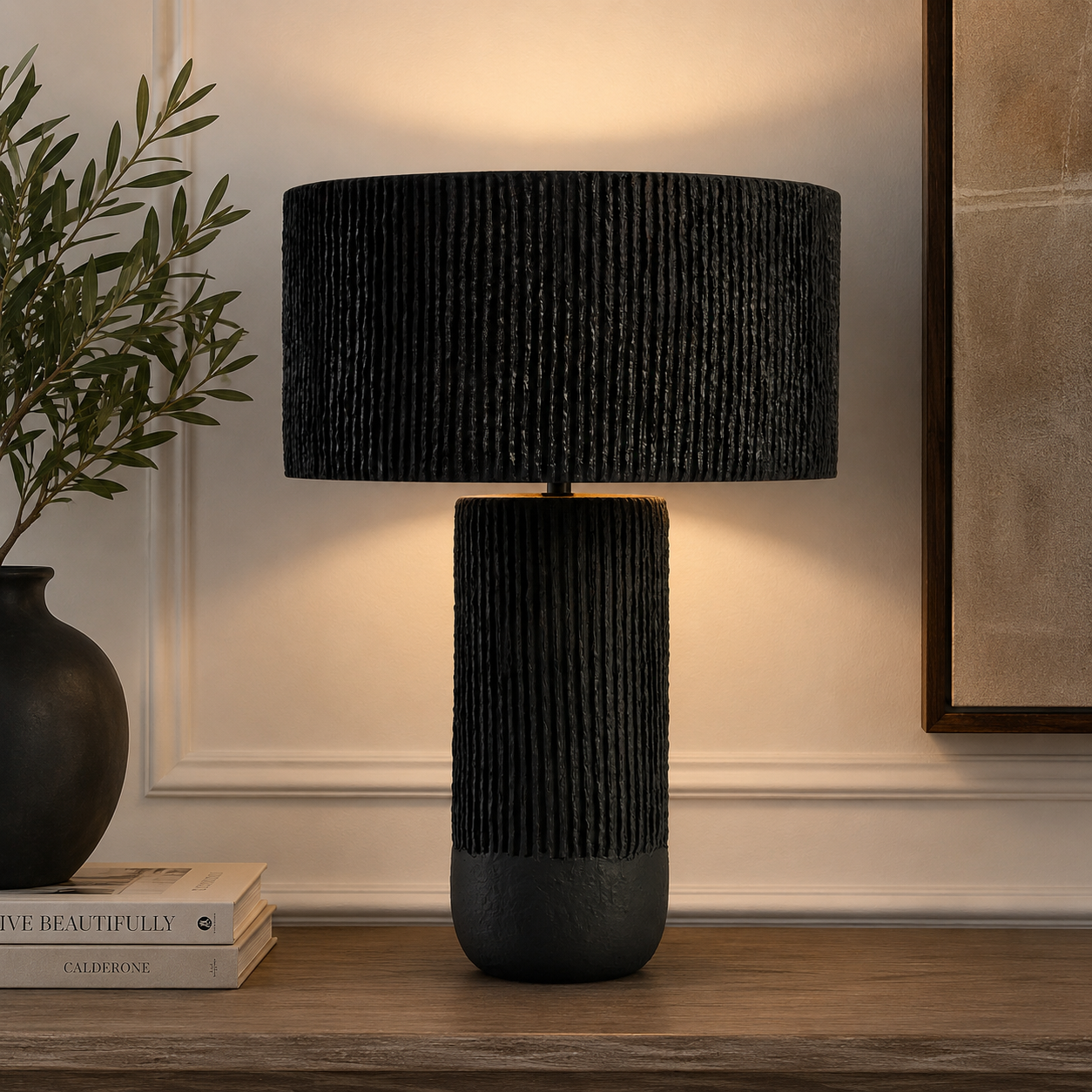 Luma black papier mache table lamp on a wooden table with decor items against a beige wall