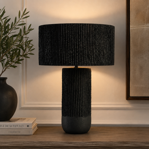 Luma black papier mache table lamp on a wooden table with decor items against a beige wall