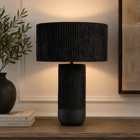 Luma black papier mache table lamp on a wooden table with decor items against a beige wall