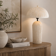 A textured cream table lamp with a ribbed cylindrical base and a matching ribbed dome shade, shown lit on a wooden console table in a styled interior setting.