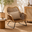 Marano black iron frame woven chair with a pillow in a cosy room setting with a plant and side table.