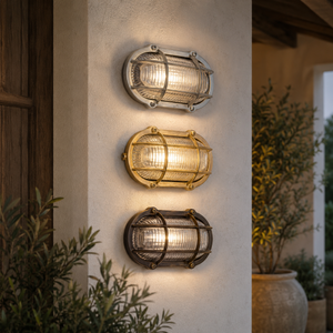Three outdoor wall sconces with ribbed glass shades mounted vertically on a stucco pillar. The top sconce has a silver-toned metal frame, the middle has a gold-toned frame, and the bottom has a dark bronze-toned frame.