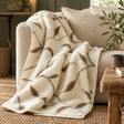 Merino Wool Leaf Pattern Blanket in cream with brown leaves draped over a linen sofa, beside a rustic wooden table, olive branches and a jute rug