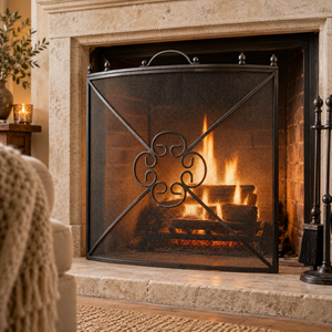 Antique pewter mesh fireguard in front of a lit open fire in a stone fire surround, with a knitted throw beside it.