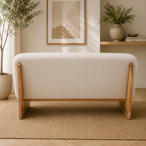 Back view of a cream linen sofa with a wooden base in a room with a woven rug and plants