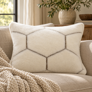 Natural Hex Cashmere Cushion with a grey hexagon pattern on a cream linen sofa with a knitted throw, beside a stone vase of olive branches