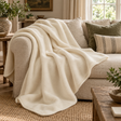 Natural Merino Wool Blanket in soft cream draped over a linen sofa with sage and striped cushions, beside a rustic wooden side table and olive branches