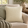 Natural Merino Wool Cushion in curly cream fleece on a linen sofa with a sage cushion and green throw, beside a stone vase of olive branches