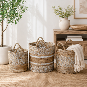 Three woven baskets on a textured surface with a plant and wooden shelf in the background.