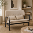 Beige linen sofa with black wood frame in a room with a woven rug and plants and decor items
