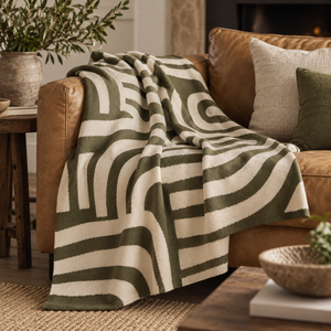 Elora Natural And Green Throw with olive arches draped over a tan leather sofa beside a stone fireplace, with linen cushions and a rustic wooden table