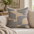 Elora Natural And Grey Square Cushion with grey embroidered blocks on a cream sofa with a knitted throw, beside olive branches in a stone vase