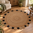 Looma Large Natural And Black Jute Rug on a wooden floor in a living room with a cream sofa, wooden cabinet and large plant pot