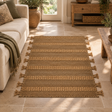 Nexo Small Striped Rug on a stone floor beside a cream sofa, with a wooden console and plants behind