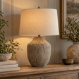 Ochre Carved Textured Table Lamp With Linen Shade lit on a wooden console beside olive branches and books