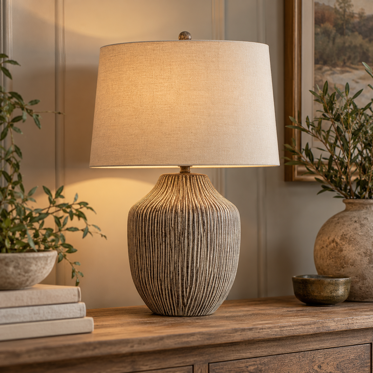 Ochre Carved Textured Table Lamp With Linen Shade lit on a wooden console beside olive branches and books