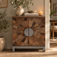 A rustic wooden sideboard cabinet with a circular wood-grain pattern on the doors and a round silver metal centre handle, styled in a warm, neutral-toned room with decorative plants, books, and a candle.