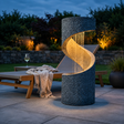 Outdoor spiral water feature with internatl lights next to a sunbed in a garden at golden hour