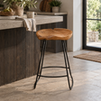 A rustic bar stool with a natural live-edge wood seat and black metal legs, positioned in a modern kitchen setting.