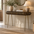 A console table with a dark brown ribbed wood top and brass legs, styled in a bright entryway with a vase of greenery, books, a lamp, and a mirror.