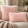 Square and rectangular Pink Curly Sheepskin Cushions on a cream sofa with a knitted throw, beside a stone vase of olive branches