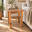 A rustic rectangular wooden end table with a distressed finish, styled in a bright living room next to a sofa with a throw blanket. The table features a light wood top and is decorated with books, a small bowl, and a vase of greenery.