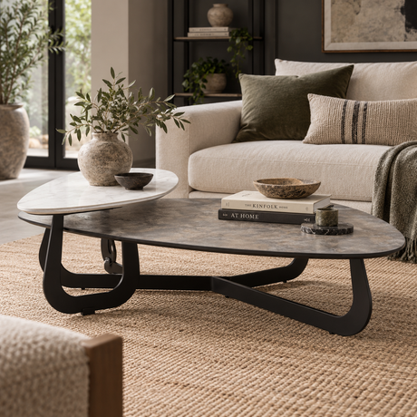 An oval coffee table in a styled living room, featuring a dark gray stone top with a black metal frame and a matching dark stone side table on top.