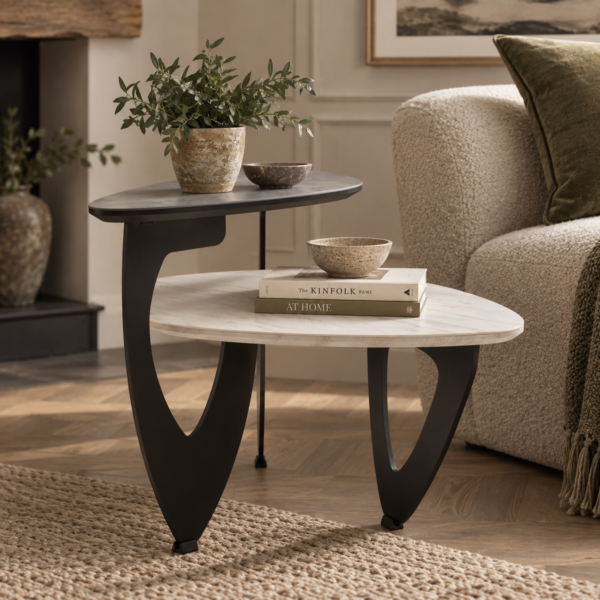A pair of nesting side/end tables in a styled living room. The larger round table has a white marble-look top and a sculptural black metal base, while the smaller oval table has a dark charcoal top and matching black base.