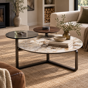 A round coffee table with a white and beige marble-patterned top and a dark metal frame, styled in a modern living room alongside two smaller nested round tables.