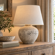Regola Large Stone Ceramic Lamp lit on a wooden chest beside olive branches and a stone bowl