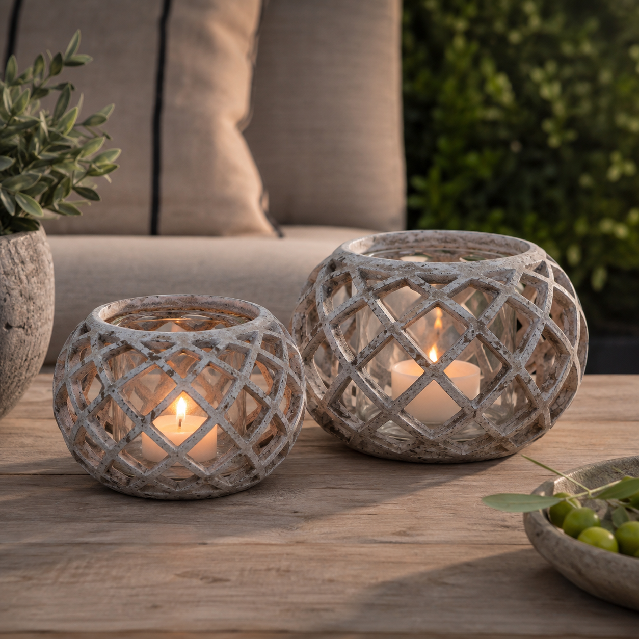Pair of round hurricane lanterns with lattice detail on an outdoor coffee table with lit candles