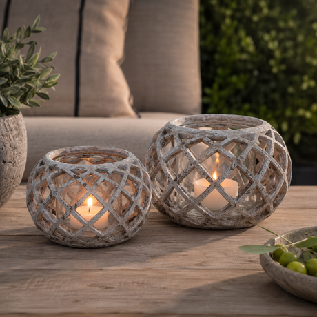 Pair of round hurricane lanterns with lattice detail on an outdoor coffee table with lit candles
